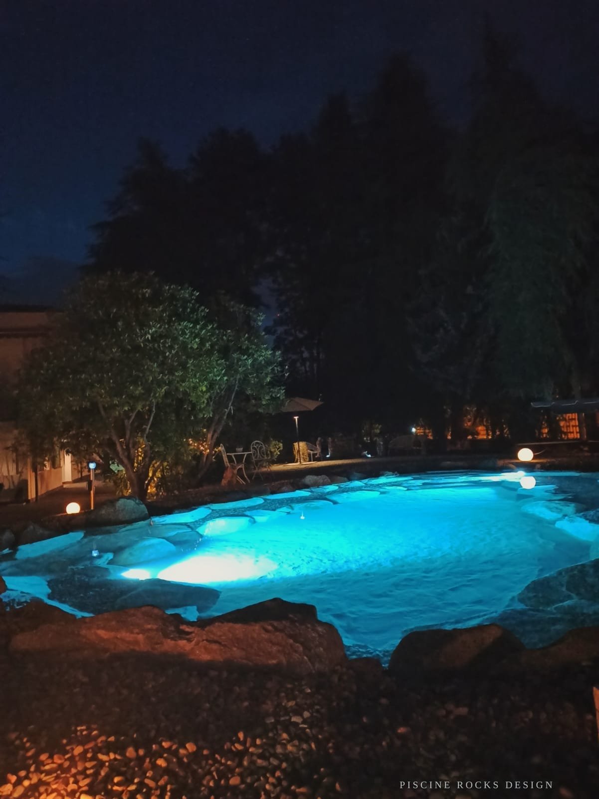 Piscina Rocks Design con illuminazione subacquea turchese di notte
